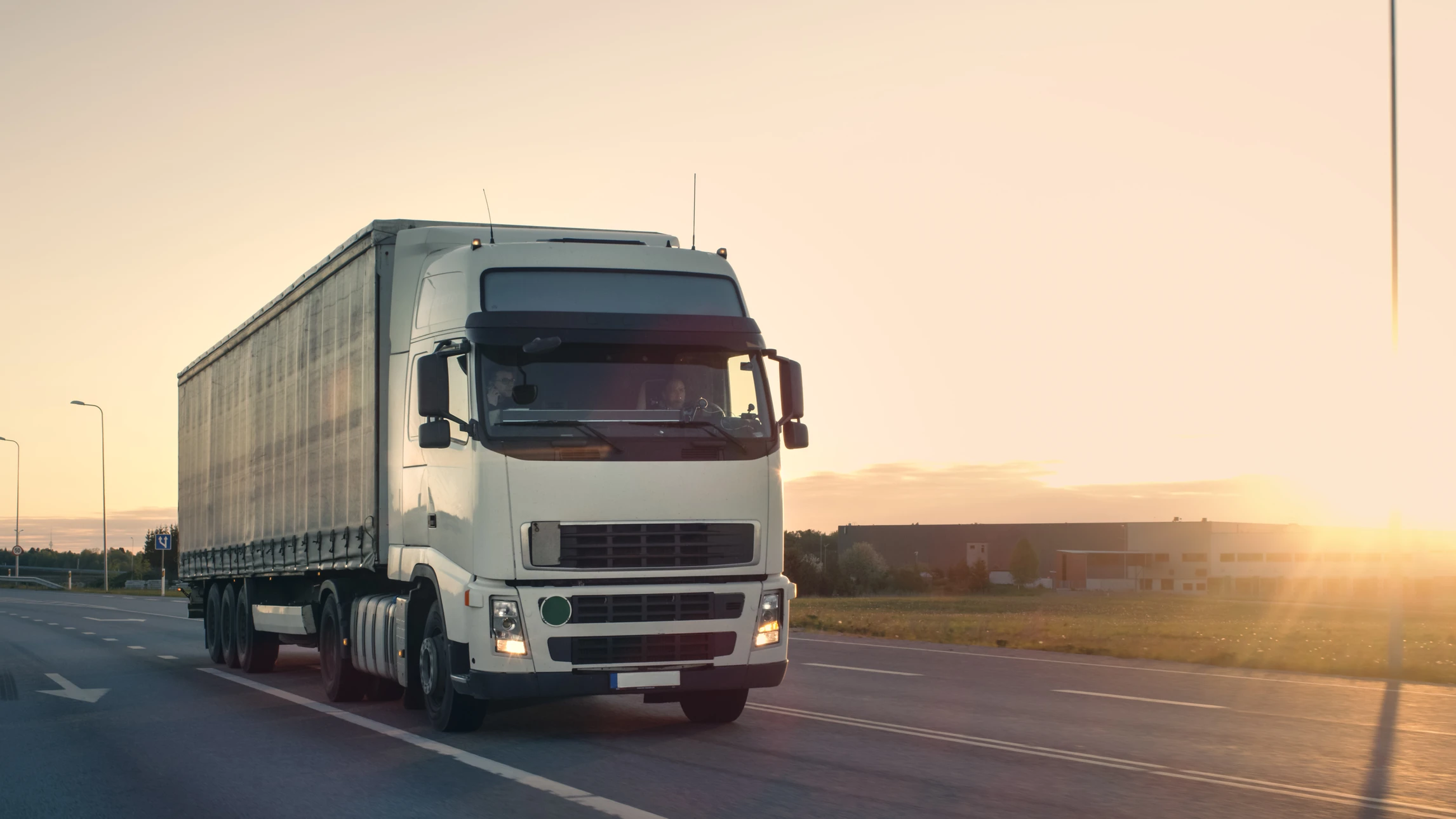Camion semi-remorque blanc circulant sur autoroute au coucher du soleil, transportant une remorque bâchée