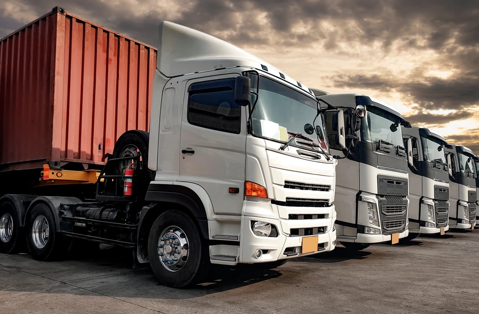Une flotte de camions blancs stationnés en rangée sur un terminal logistique au coucher du soleil
