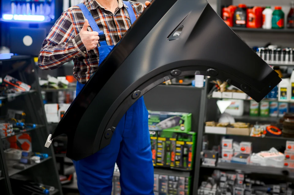Photographie d'un professionnel de la distribution automobiles en environnement de showroom ou d'accueil client, écoutant attentivement un client en lui expliquant les caractéristiques d'une pièce détachée automobile (moteur, filtre, batterie ou autre composant courant). Le professionnel peut être en train de consulter un ordinateur ou un catalogue technique pour identifier la bonne référence. L'atmosphère doit être professionnelle, courtoise et montrer clairement l'interaction conseil et l'expertise mise au service du client pour trouver la solution adaptée.