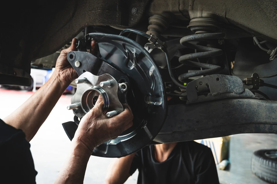 Professionnel exp&eacute;riment&eacute; en tenue professionnelle dans un atelier ou un espace de stockage, examinant attentivement des pi&egrave;ces d&eacute;tach&eacute;es automobiles vari&eacute;es (moteur, filtres, courroies, plaquettes de frein, alternateurs, etc.) organis&eacute;es sur des &eacute;tag&egrave;res ou un &eacute;tabli. L'atmosph&egrave;re doit &ecirc;tre celle d'un expert qualifi&eacute; ma&icirc;trisant sa s&eacute;lection de pi&egrave;ces neuves de qualit&eacute;, loin de l'atmosph&egrave;re commerciale de concession automobile. &Eacute;clairage professionnel, environnement technique et organis&eacute;, refl&eacute;tant 35 ans de ma&icirc;trise du m&eacute;tier de distribueur de pi&egrave;ces.